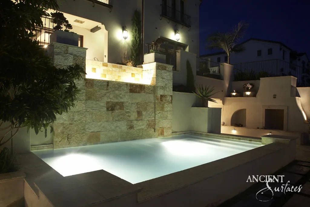 Illuminated pool framed by reclaimed limestone cladding and paving at night