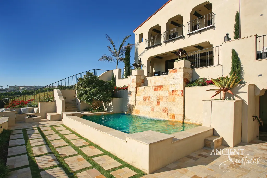 Reclaimed limestone pool coping and a clad water wall beside an infinity pool at a sunlit Laguna Beach villa