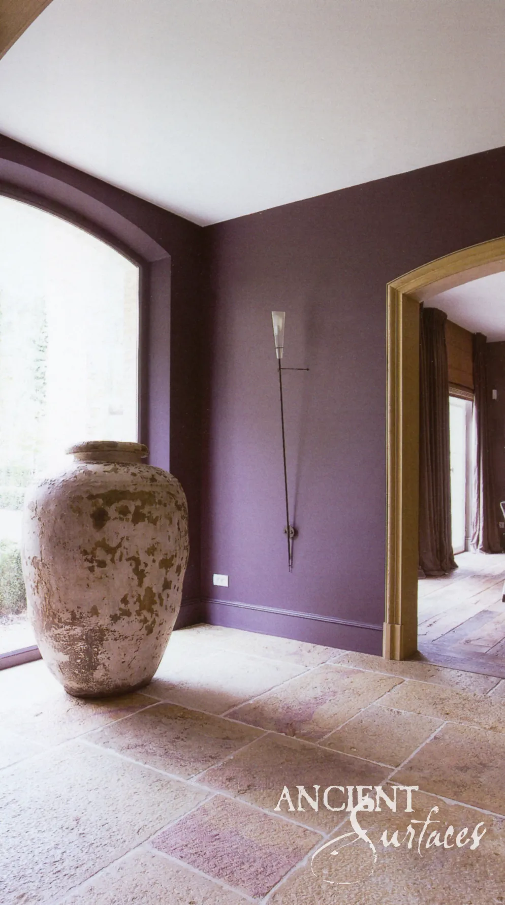 Antique stone urn on a reclaimed limestone floor against a deep plum wall