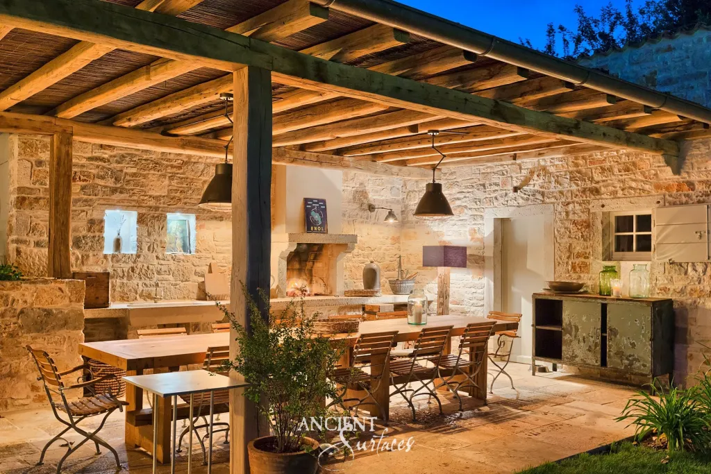 Reclaimed antique limestone outdoor dining terrace beneath a timber pergola at dusk
