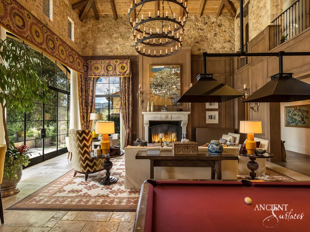 Grand great room with a hand-carved limestone fireplace, antique stone floor, and iron chandelier